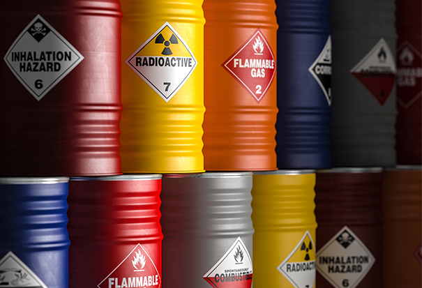 A stack of two rows of chemical barrels of varying colors, identified with diamond warning labels, indicating various health hazards.