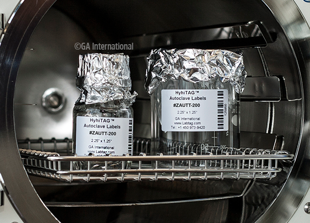 two containers being pulled out of the autoclave machine. they are labelled with the high-temperature resistant labels, printed with information an a barcode